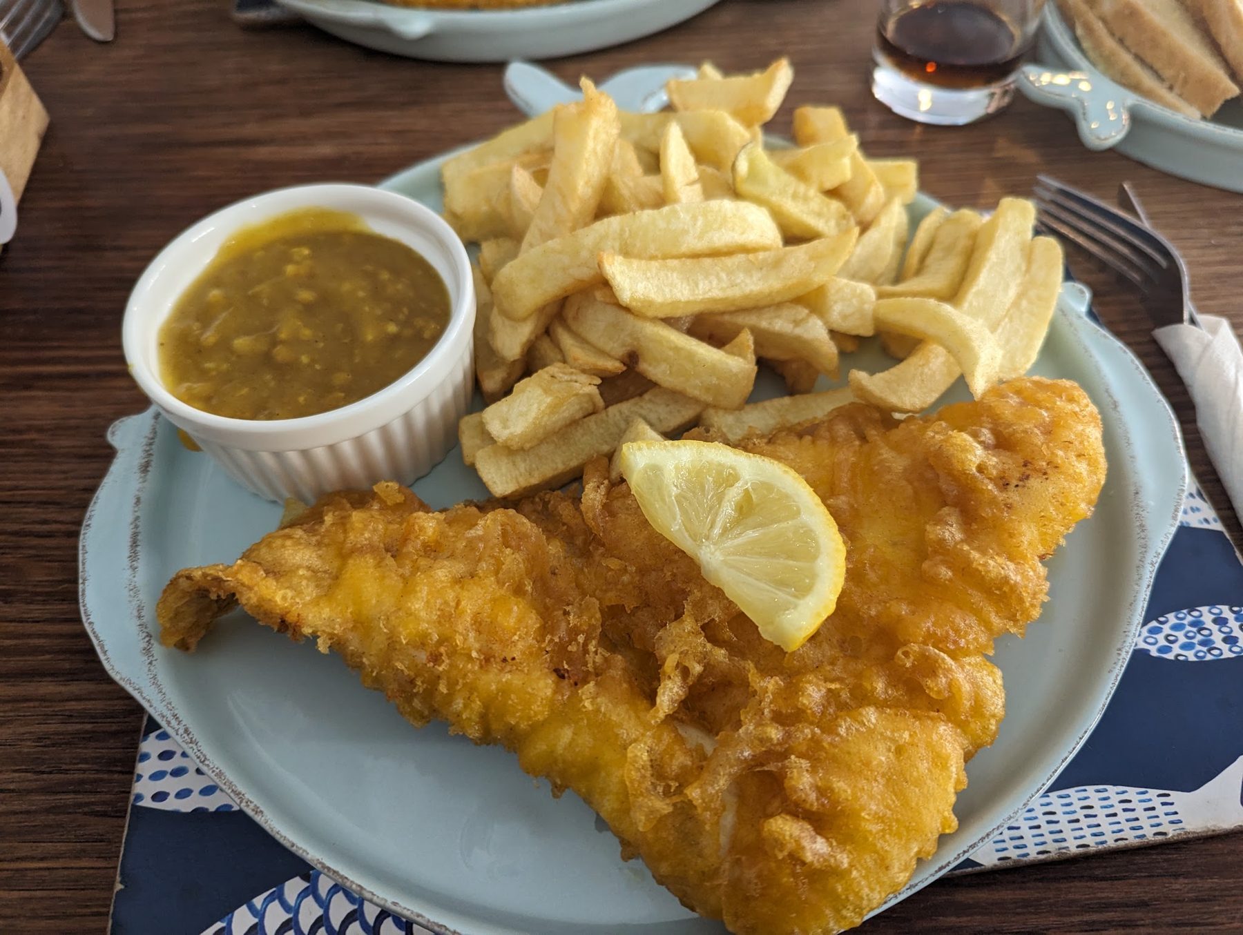 Battered fish and chips with a lemon wedge and a pot of curry sauce